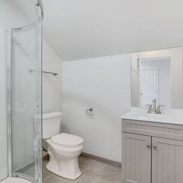 Renovated bathroom with a curved glass corner shower and grey vanity